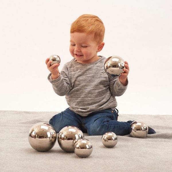 Un niño pequeño sentado en el suelo jugando con bolas de plata, una foto de stock de Sara Saftleven, destacada en Pinterest, arte cinético, trazado de rayos, hecho de metal líquido, trazado de Vray.