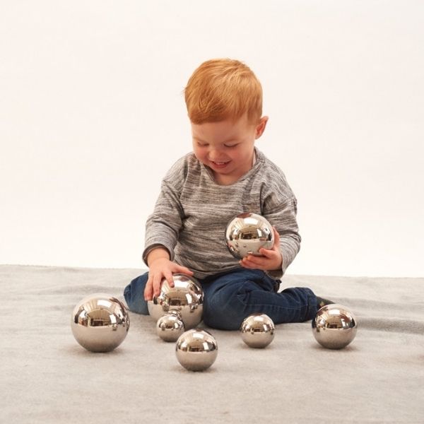 Un joven sentado en el piso jugando con bolas de plata, una foto de stock de Cornelia Parker, destacada en Pinterest, arte cinético, trazado de rayos, fotografía de estudio, vray trazado.