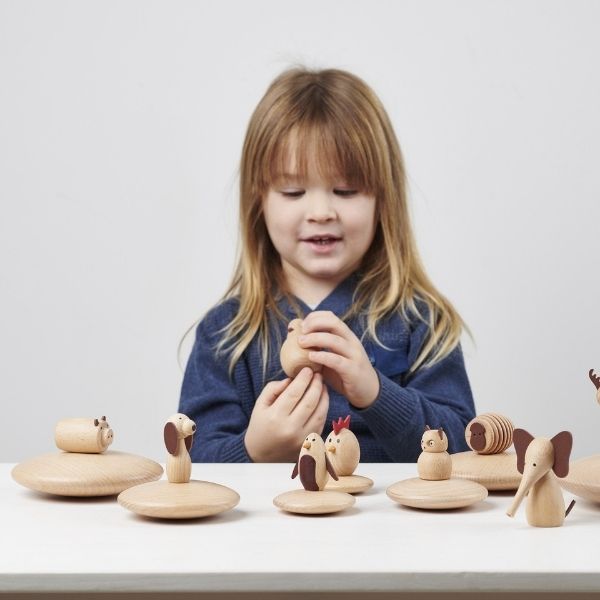 Una niña pequeña jugando con animales de madera en una mesa, un rompecabezas de Gwilym Prichard, destacado en la sociedad CG, movimiento de artesanía, patrón repetitivo, profundidad de campo poco profunda, hecho de cartón.