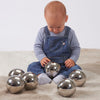 Una bebé sentada en el suelo jugando con bolas de plata, una foto de stock de Anne Geddes, tendencia en Pinterest, fluxus, trazado de rayos, fotografía de estudio, hecha de metal líquido.