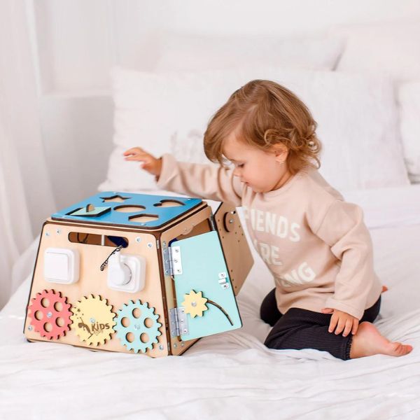 Una niña pequeña jugando con un juguete en una cama, un rompecabezas de Eden Box, ganador del concurso de Pinterest, Los Automatistas, Adafruit, hecho de cartón, ganador del concurso.