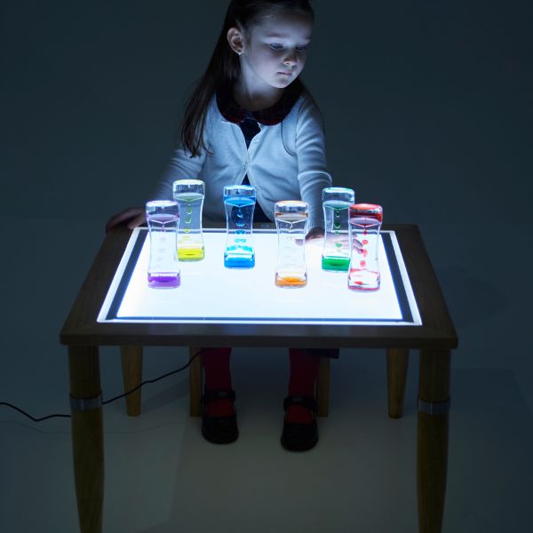 Una niña sentada en una mesa con una superficie iluminada, un holograma de Cerith Wyn Evans, presentado en la Sociedad de CG, arte interactivo, bioluminiscencia, luminiscencia, arte académico.