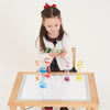 Una pequeña niña sentada en una mesa jugando con tazas de colores, un holograma de Keos Masons, presentado en la Sociedad CG, arte cinético, fotografía de estudio, luz de estudio, trazado de ondas cuánticas.