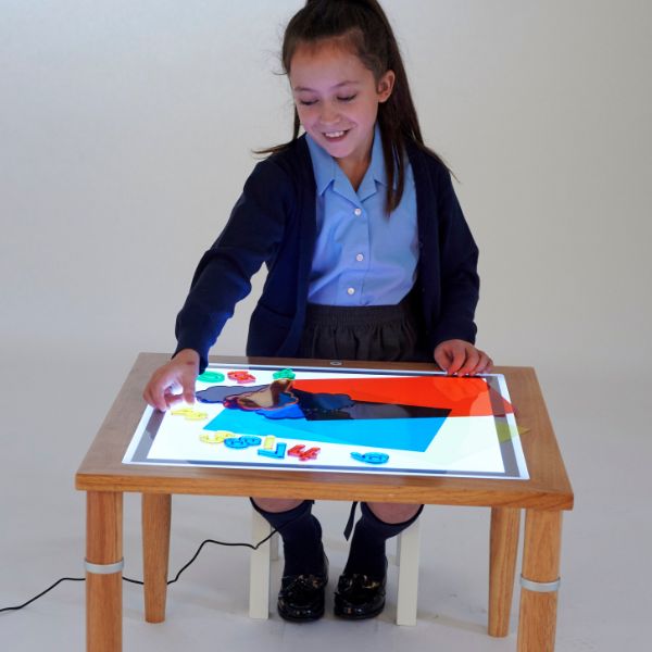 Una niña pequeña sentada en una mesa con una foto en ella, un holograma de Sarah Morris, destacado en dribble, arte interactivo, tecnología futura, arte de juegos 2D, dibujo de un niño.
