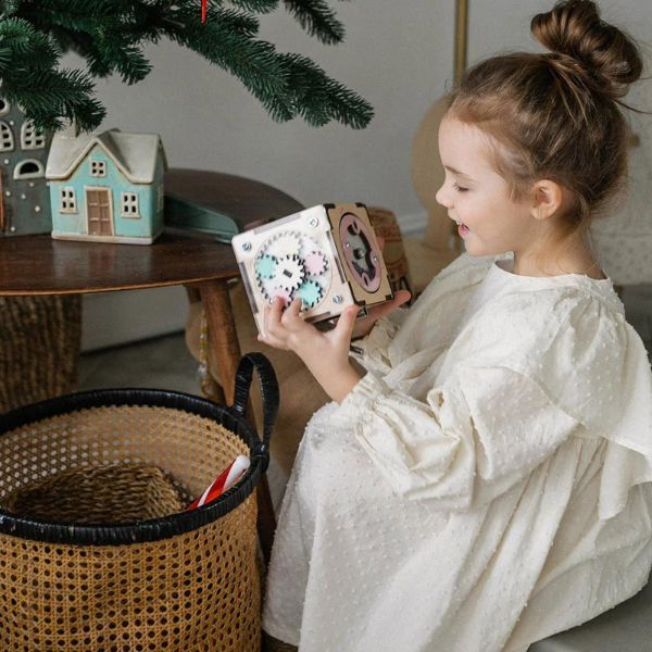Una niña pequeña sentada en un sofá sosteniendo una caja, un bordado cruzado por Ottilie Maclaren Wallace, ganador del concurso de Instagram, arte popular, patrón repetitivo, caprichoso, lleno de detalles.
