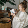 Una niña pequeña sentada en un sofá sosteniendo una caja, un bordado cruzado por Ottilie Maclaren Wallace, ganador del concurso de Instagram, arte popular, patrón repetitivo, caprichoso, lleno de detalles.