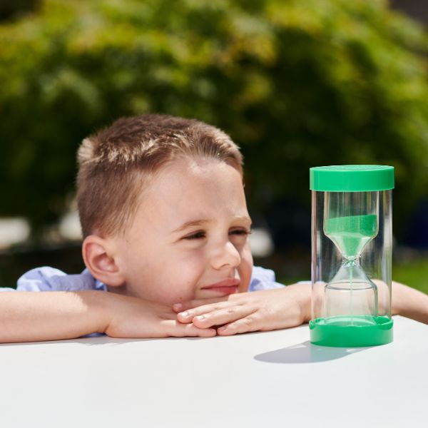Un pequeño niño sentado en una mesa con un reloj de arena verde, una foto de stock por Elizabeth Durack, ganador del concurso de Instagram, les Automatistes, foto de stock, profundidad de campo, foto de stock.