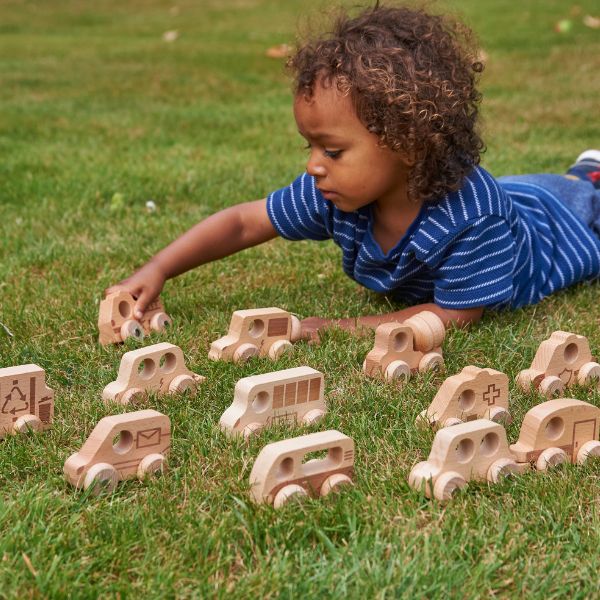 Una niña joven jugando con juguetes de madera en la hierba, una foto de stock de Jeanna Bauck, destacada en dribble, movimiento de artes y manualidades, profundidad de campo, profundidad de campo poco profunda, patrón repetitivo.