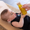 Una bebé sentada en un banco de madera sosteniendo una botella, una foto de stock de Else Alfelt, destacada en dribble, dada, foto de stock, foto de stock, brillo.