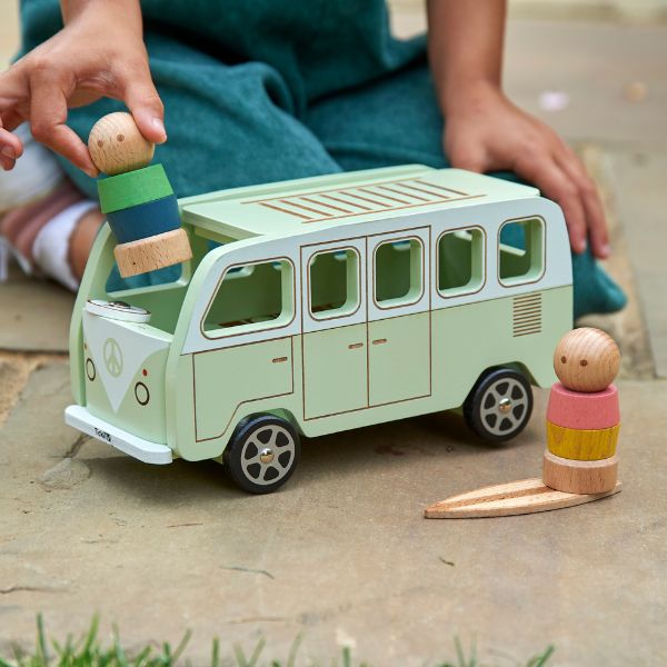 Una niña jugando con un autobús de juguete de madera, una ilustración de un libro de cuentos de Annabel Kidston, presentado en dribble, movimiento de artesanía, hecho de cartón, fantástico, ilustración de un libro de cuentos.